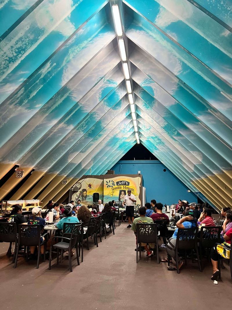 A full house of guests at tables inside the A-Frame, under its turquoise wave-painted ceiling