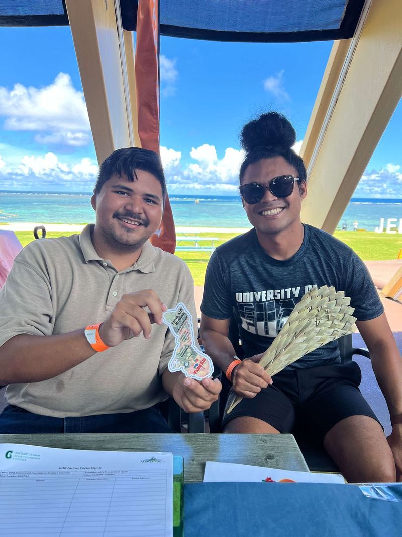 Two smiling guests at a booth in the open-air pavilion, the turquoise Pacific right behind them
