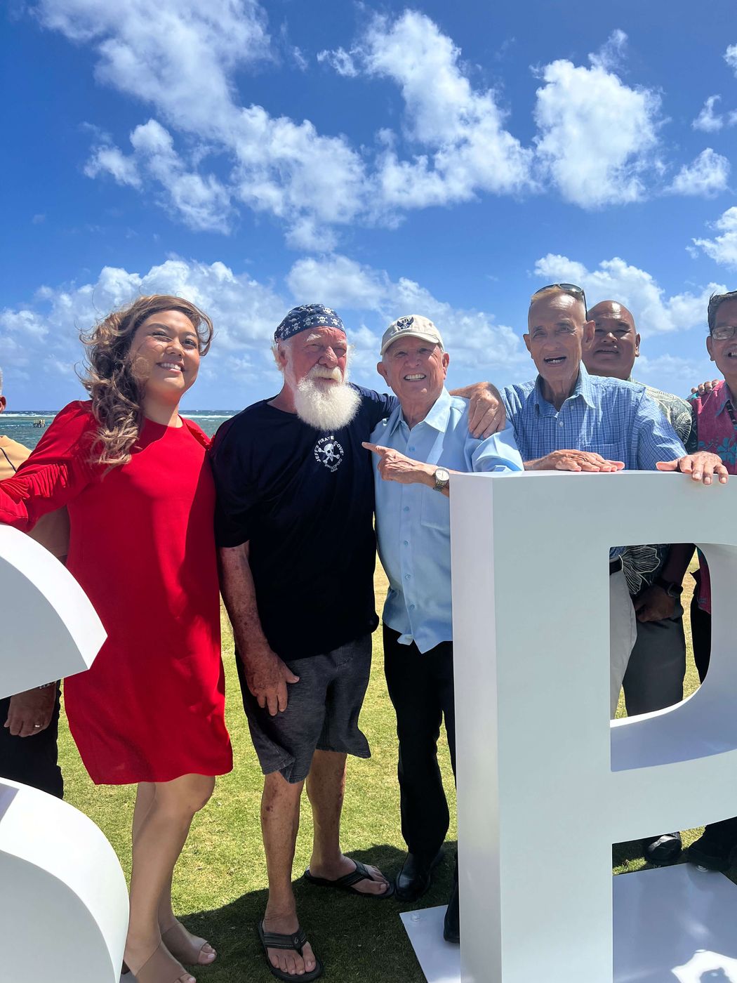 Pirate Captain Jeff and guests smiling beside the giant white letters on the oceanfront lawn, blue sky and the Pacific behind