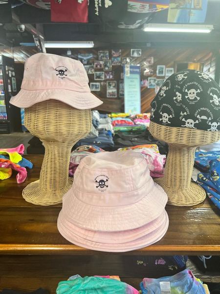 Pale pink bucket hats with a small skull logo and a skull-print cap on wicker stands