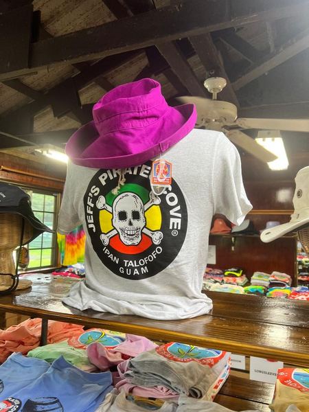 A white JPC logo tee and a magenta sun hat on a mannequin