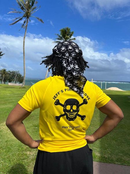 The back of a yellow JPC tee with the skull and crossbones, worn outdoors