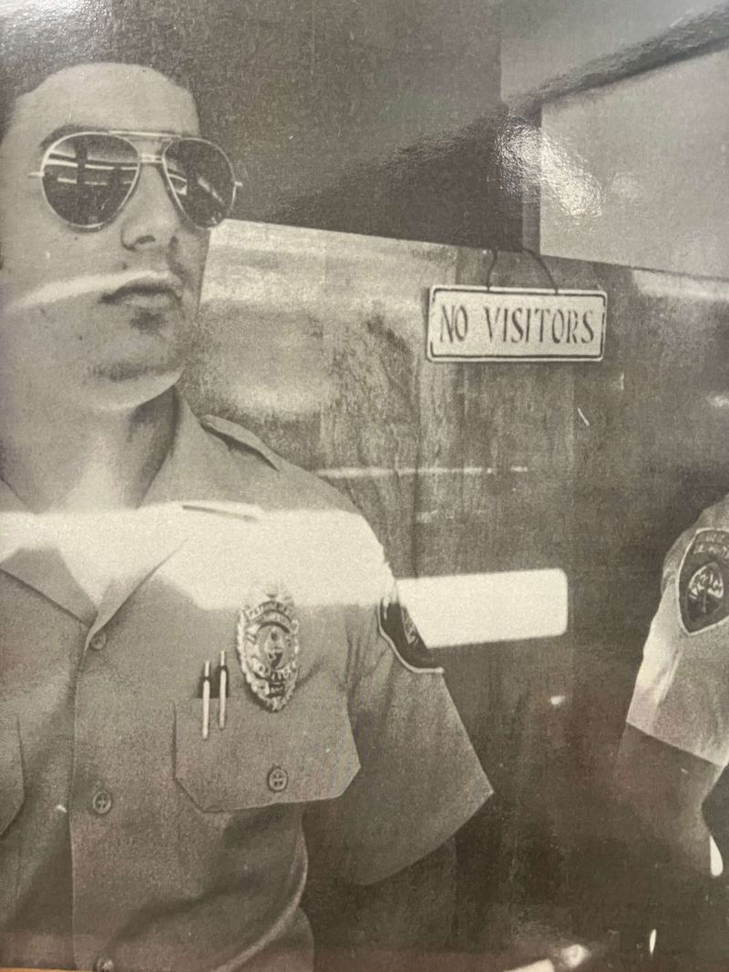 A uniformed officer in sunglasses beside a No Visitors sign